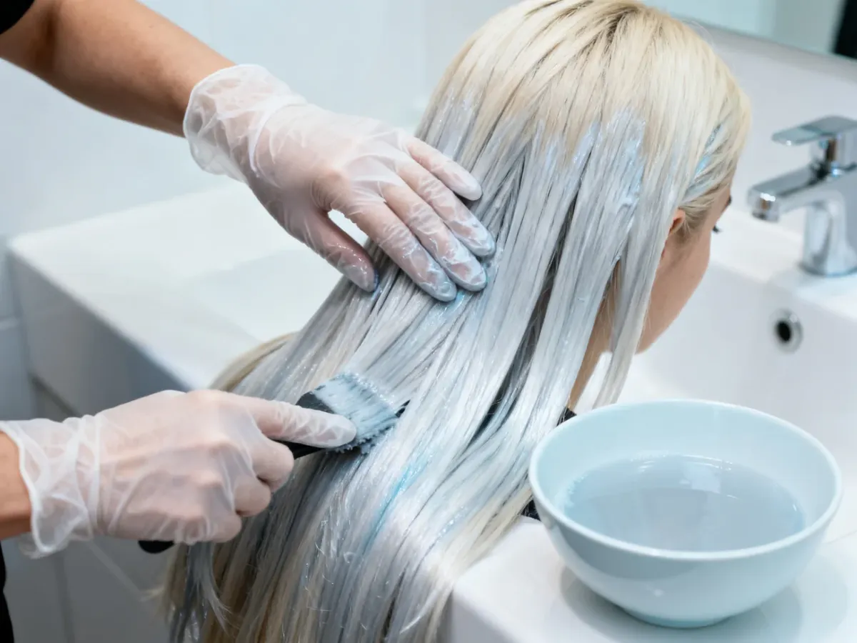 Nakładanie srebrnej płukanki na wilgotne blond włosy w rękawiczkach